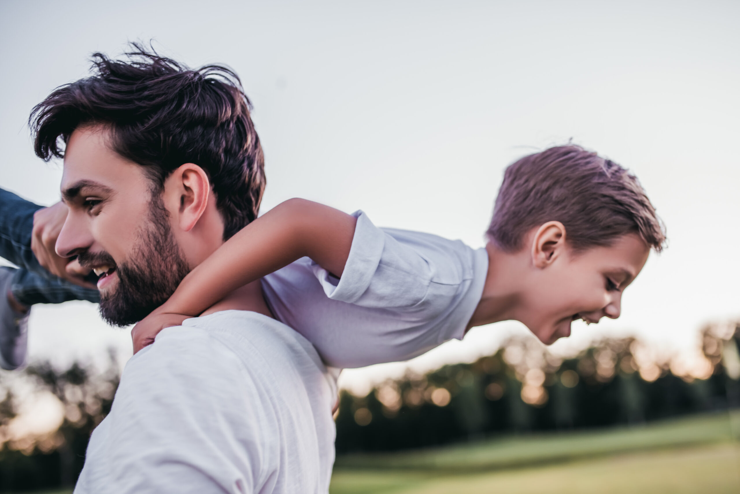 Young boy and adult having fun outdoors with child over adults shoulder